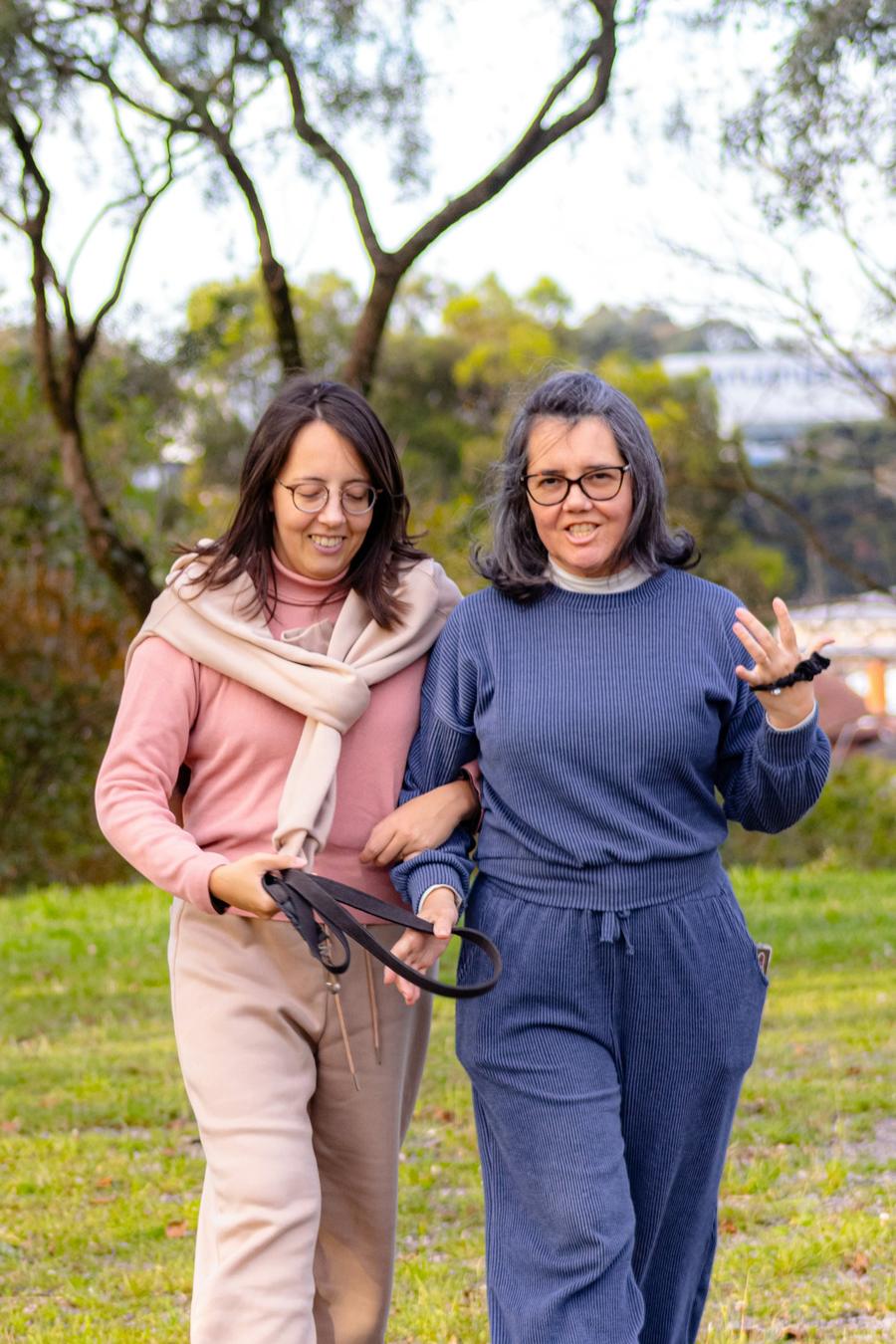 Two women walking arm in arm across a sunny park lawn